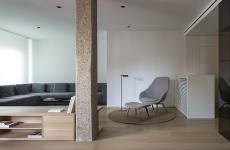 Contemporary open-plan living space with minimalist furniture, stone column, and wood accents.