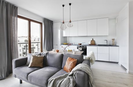 Modern kitchen and living area with white cabinets, gray couch, and pendant lighting.