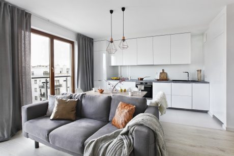 Modern kitchen and living area with white cabinets, gray couch, and pendant lighting.