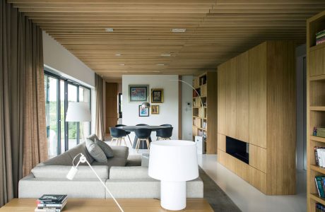 A minimalist living room with a wood-paneled ceiling, neutral furniture, and built-in storage.