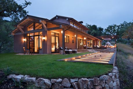 Rustic wood-and-stone lodge-style home with grand covered porch, patio, and landscape lighting.