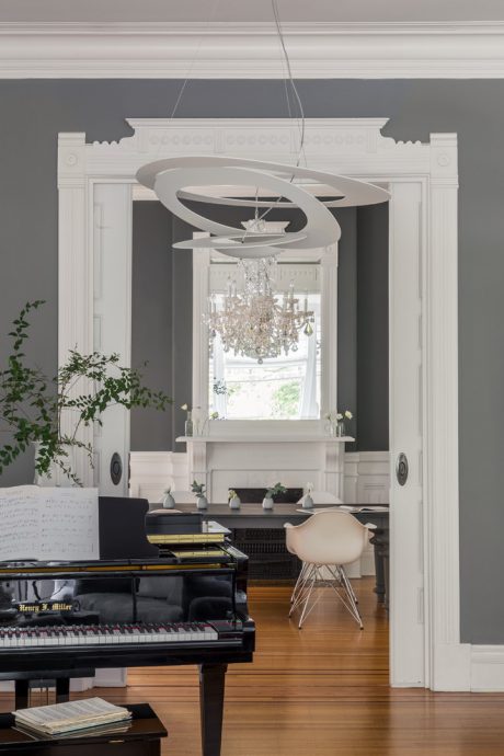 A grand living room with ornate moldings, a crystal chandelier, and a grand piano.