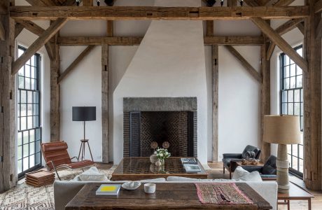 Rustic, open-concept living space with exposed wooden beams and large fireplace.