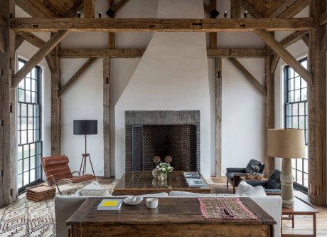 Rustic, open-concept living space with exposed wooden beams and large fireplace.