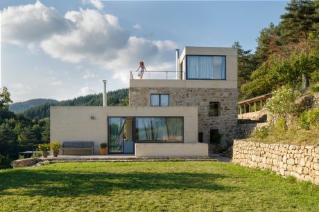 Contemporary mountain residence with stone exterior, large windows, and balcony.