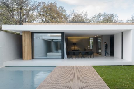 Modern, minimalist architecture with large glass windows, wooden accents, and a pool in the foreground.