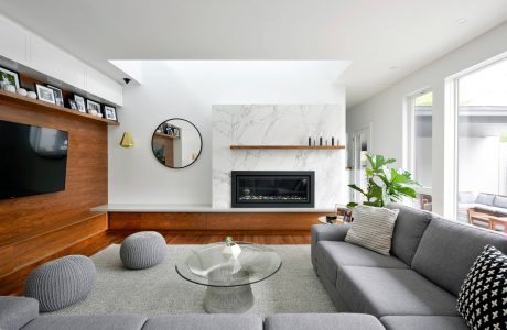 Stylish, contemporary living room with marble fireplace, wooden wall units, and plush grey seating.