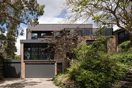 Modern, minimalist home with glass windows, brick exterior, and lush greenery surrounds.