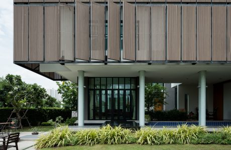 A modern architectural design featuring wooden slat panels, glass walls, and lush greenery.