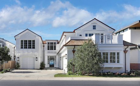 Elegant two-story home with white siding, triangular dormers, and a spacious porch.