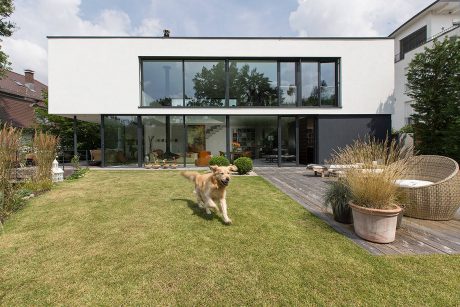 Modern glass-enclosed home with expansive yard and lush landscaping.