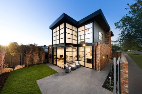 A modern glass-walled home with sleek lines, brick exterior, and cozy outdoor seating.