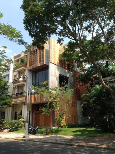 An elegant multi-story building with intricate wood and glass facade, surrounded by lush greenery.