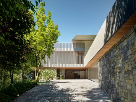 A modern architectural design featuring a sleek exterior with stone walls, angled roofs, and lush landscaping.