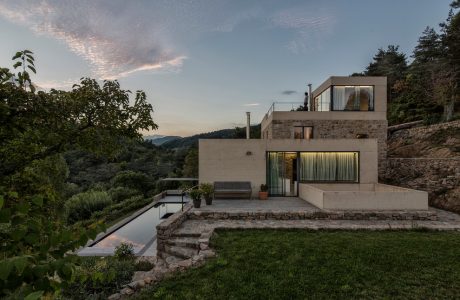 Striking modern architecture with glass walls, stone exterior, and serene pond.