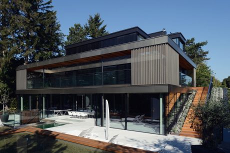 Modern, multi-level home with glass walls, wooden accents, and an elevated terrace.