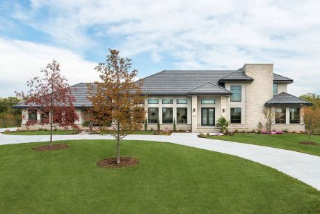 Spacious single-story home with brick and glass facade, slanted roof, and manicured lawn.