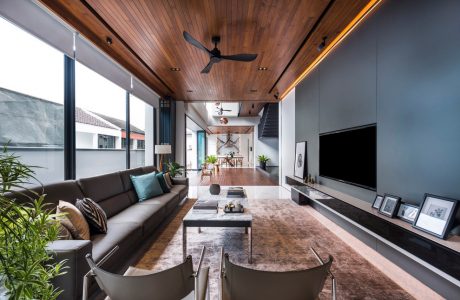 A modern open-plan living space with a wooden ceiling, large windows, and a ceiling fan.