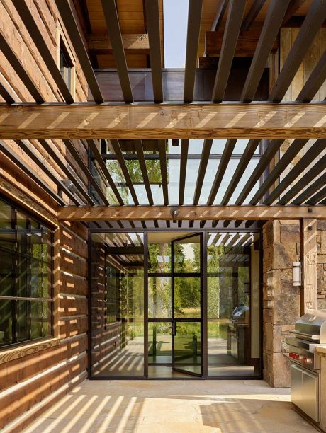 Rustic architectural details, including exposed wooden beams and large glass doors overlooking nature.