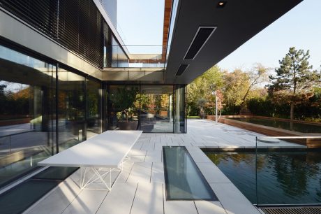 A sleek, modern residential design featuring glass walls, a pool, and an open outdoor space.