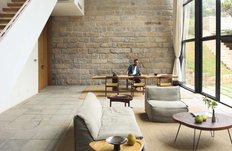 Minimalist living room with exposed brick wall, wooden furniture, and large windows.