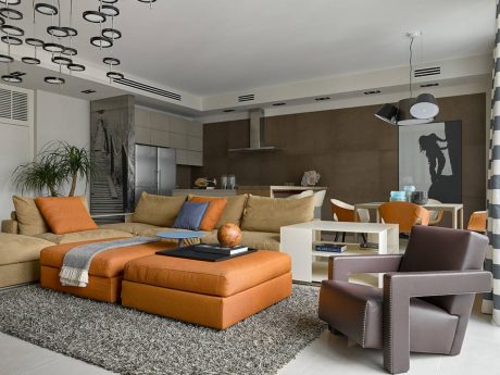 Modern living room with plush orange sectional, artwork, and pendant lighting.