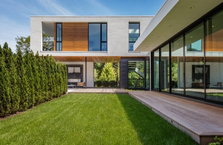 Sleek modern facade with expansive glass panels, wooden accents, and well-manicured yard.