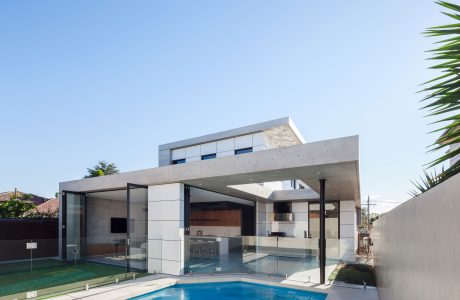Modern, open-concept house with pool and glass walls overlooking lush greenery.
