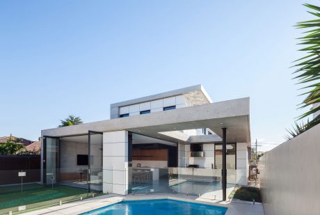 Modern, open-concept house with pool and glass walls overlooking lush greenery.
