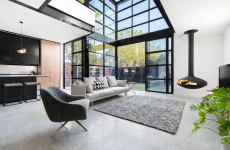 Modern glass and steel interior with sleek furniture, fireplace, and views of the outdoors.
