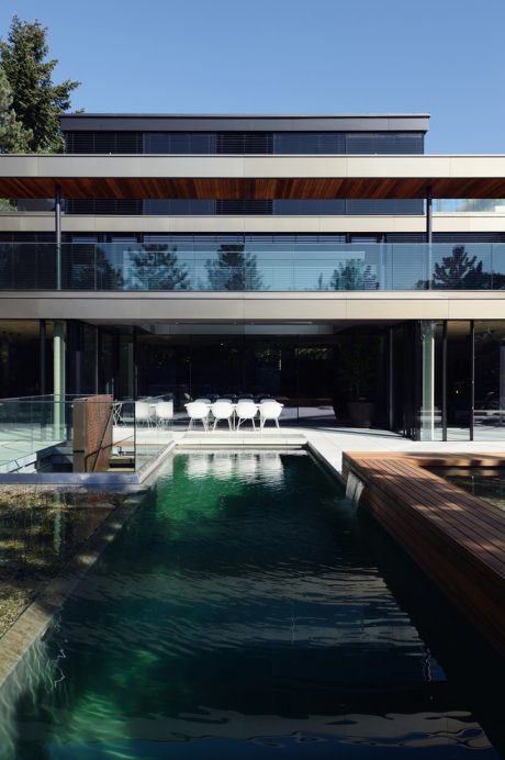 Glass-enclosed modern residence with wooden deck, pool, and minimalist decor.
