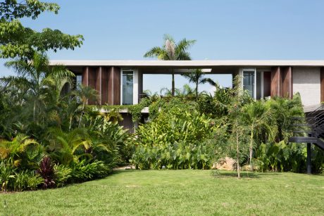 A modern tropical villa with a lush, verdant garden and palm trees surrounding it.