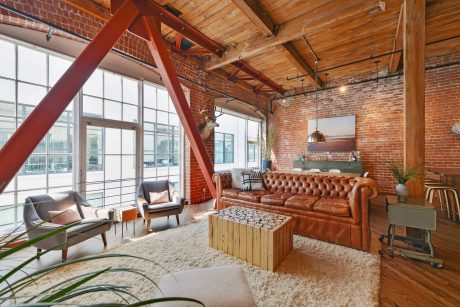 Spacious loft-style room with exposed brick walls, wooden beams, and a large leather sofa.