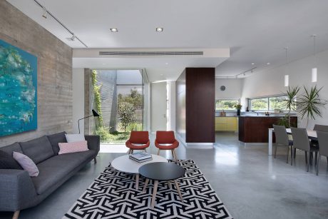 Spacious modern living room with concrete walls, large windows, and a geometric area rug.