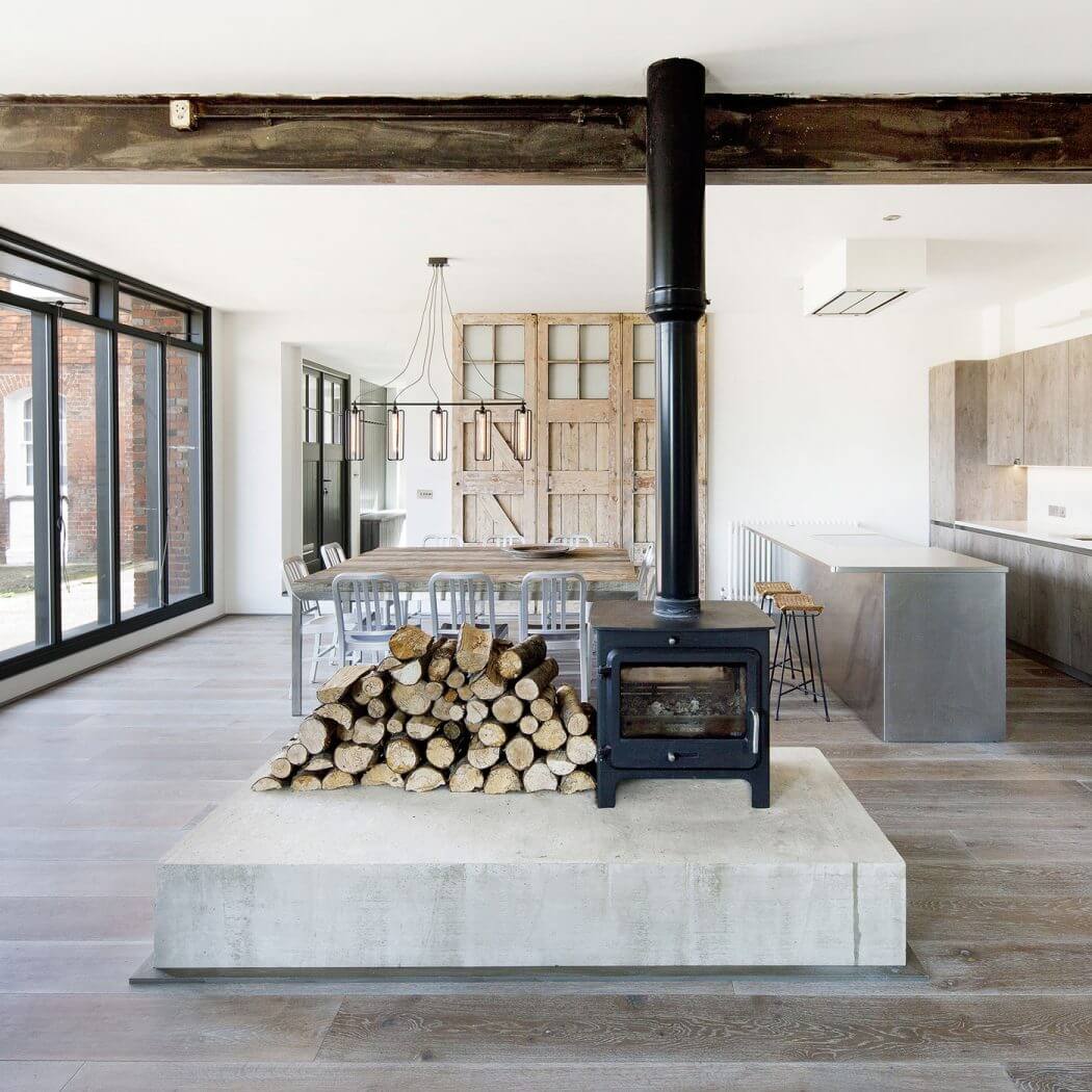 A modern, loft-style interior featuring a wood-burning stove, rustic wood furnishings, and industrial lighting.