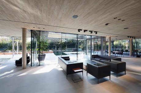 A modern, open-plan interior with glass walls, concrete ceiling, and minimalist furniture.