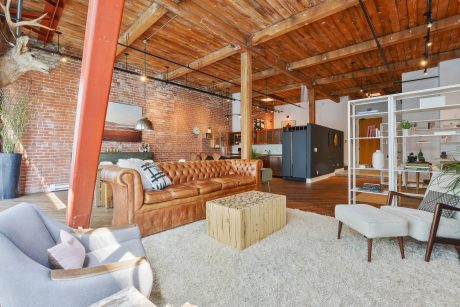 Open-concept loft with exposed brick walls, wooden beams, and a plush leather sofa.