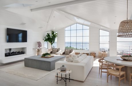 Large, bright open-concept living room with white walls, vaulted ceiling, and panoramic windows.