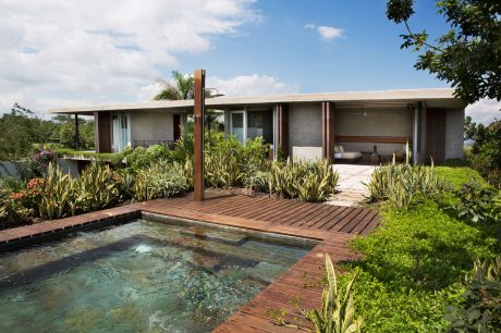 Sleek, modern home with a wooden deck and a serene pool surrounded by lush greenery.