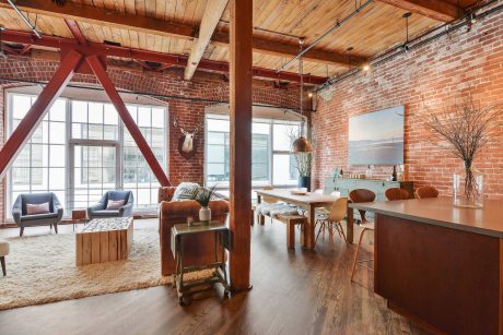 An open-concept loft with exposed brick walls, wooden beams, and a mix of modern and rustic furnishings.