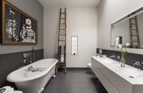 A spacious bathroom with an antique-style bathtub, stained glass window, and decorative ladder.