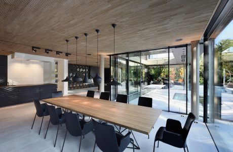 Minimalist dining area with wooden table, black chairs, and large glass windows overlooking outdoor space.