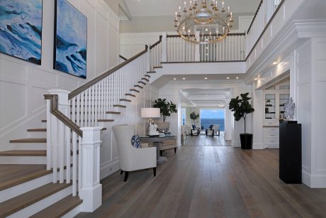 Elegant foyer with grand staircase, ornate chandelier, and coastal-inspired artwork.
