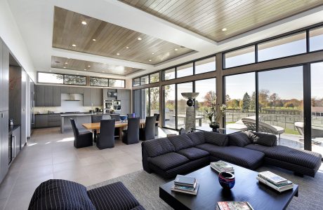 Spacious open-concept living area with large windows, wood-paneled ceiling, and modern furnishings.