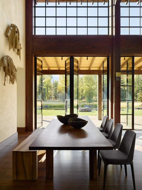 Expansive windows offer panoramic views of the natural scenery. Wooden beams and modern furnishings create a cozy, rustic ambiance.
