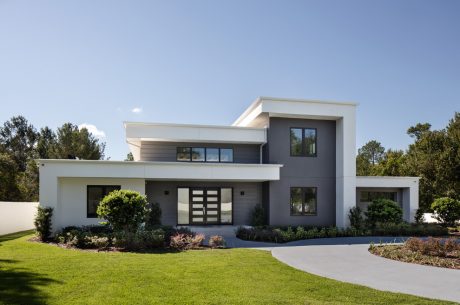 Modern two-story house with sleek, angular design, large windows, and lush landscaping.