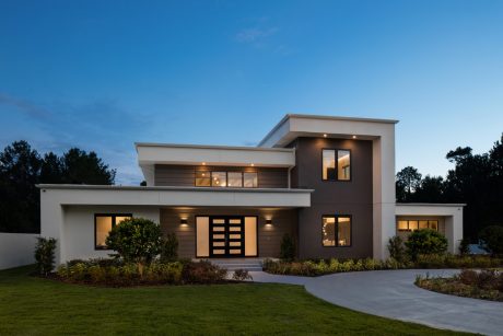 Modern two-story house with clean lines, large windows, and illuminated exterior.