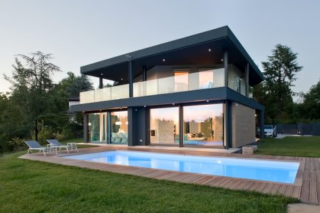 Modern two-story home with a glass facade, balcony, and a sleek pool in the backyard.