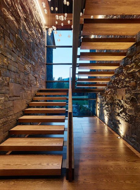 Elegant wooden staircase against stone walls, suspended glass lighting fixtures.