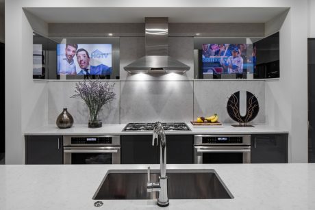 Modern kitchen with sleek stainless steel appliances, recessed lighting, and mounted TVs.